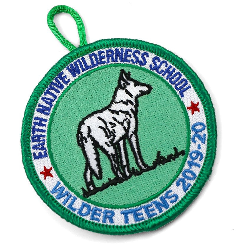 Green, blue, white, black and red embroidered scout patch with wolf graphic and text: Earth Native Wilderness School, Wilder Teens 2019-20.